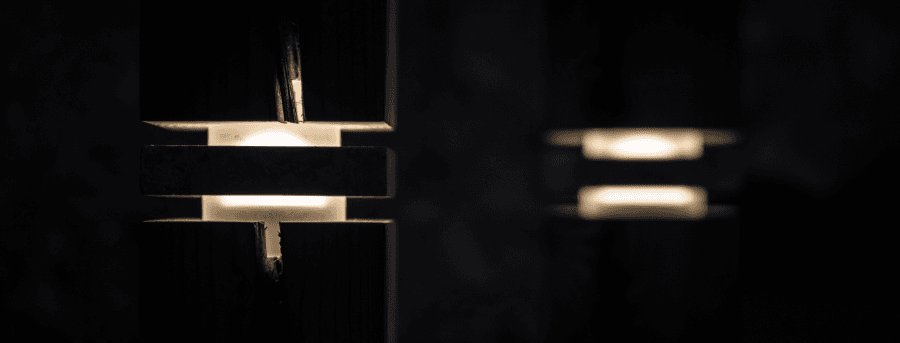 Vaial dettaglio luce Luce che esce da due tagli orizontali tra legno e pietra in una stanza scura.