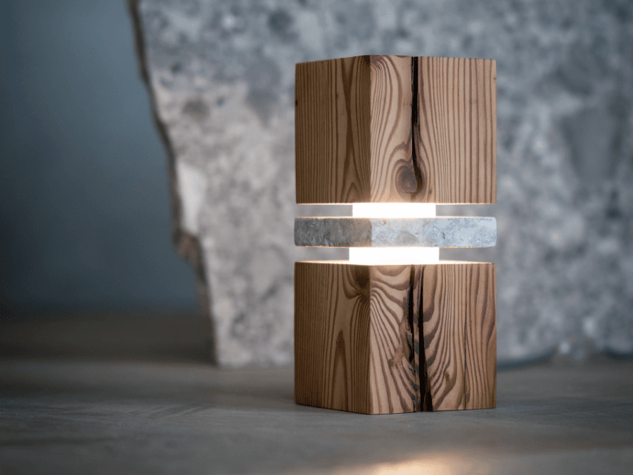 Vaia lampada singola Immagine della lampada Vaia costituita da due blocchi di legno e un ripiano di pietra fluttuante su uno sfondo di pietra grigia.
